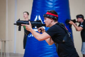 Игрок LASERWAR с автоматом в прицеле у синего препятствия.